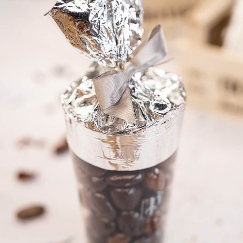 Zoom sur un cône d'Amandas Avelinas de la chocolaterie Puyricard renversé sur le côté et son couvercle en aluminium déchiré, laissant se déverser des amandas.