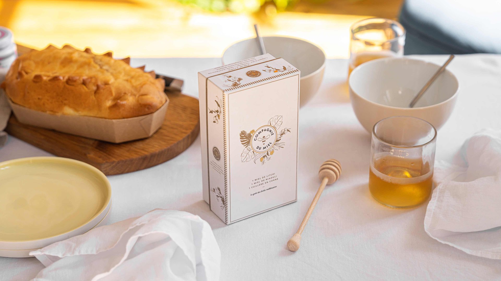 Box of honey with special spoon on the table with napkin, dishes, cake