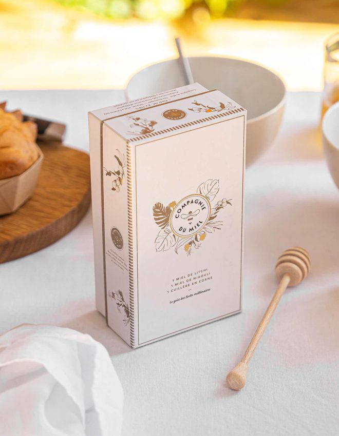 Box of honey with special spoon on the table with napkin, dishes, cake