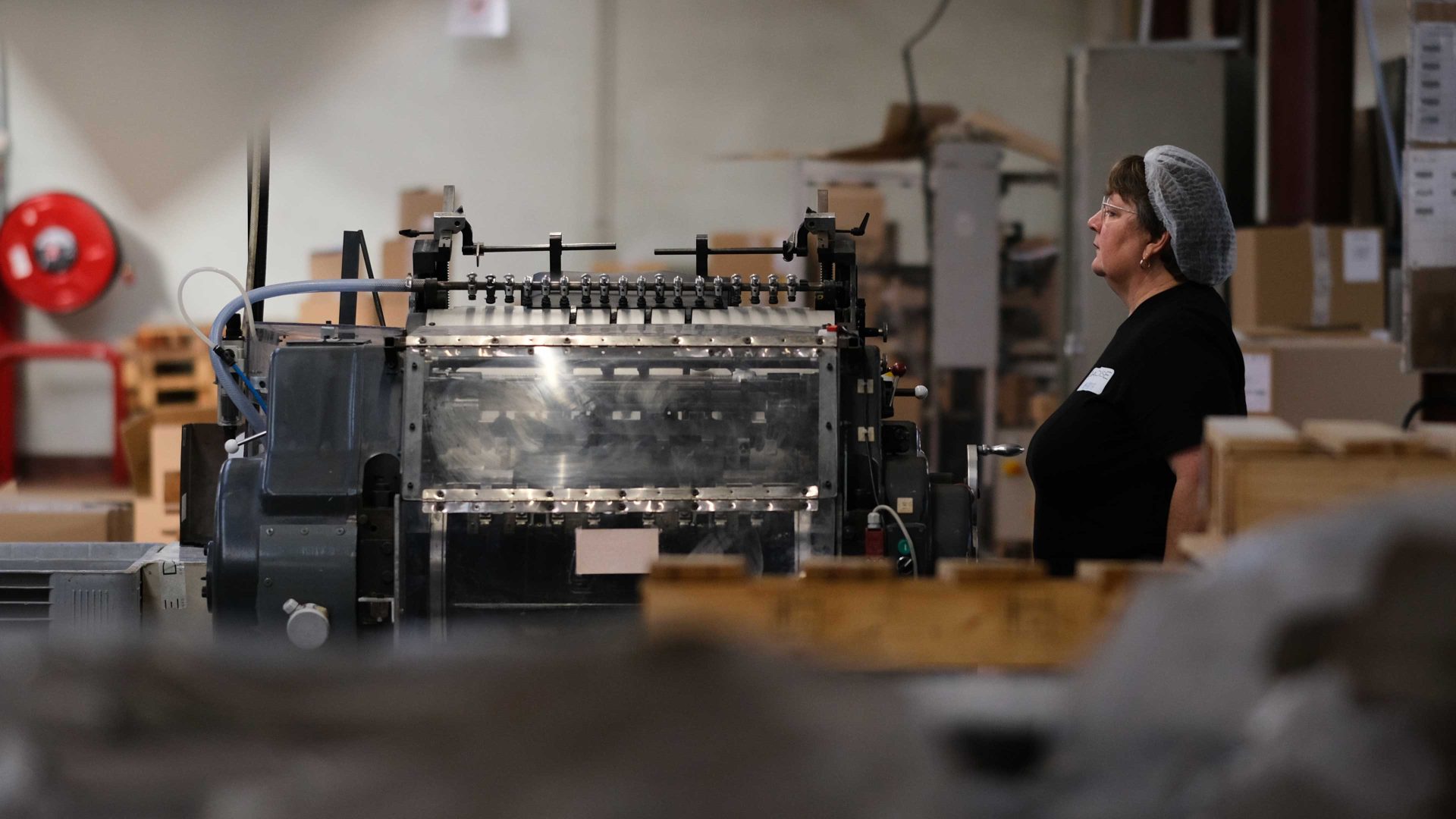 Une femme portant un filet de protection, se trouve derrière une machine dans un atelier de production et regarde au loin