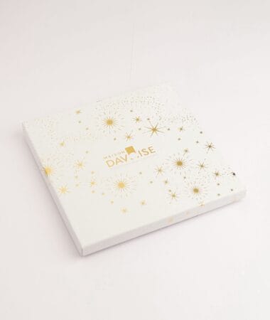 Boîte carrée Maison Davaïse blanche décorée d’étoiles dorées, fermée sur fond neutre.
