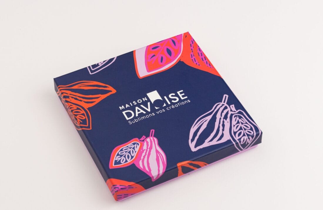 Boîte carrée Maison Davoise bleu nuit ornée d’illustrations de cabosses stylisées.